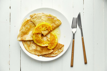 Overhead image of french crepes with orange confiture in white plate on wooden table