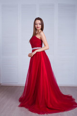 Beauty brunette model woman in red evening dress. Beautiful fashion luxury makeup and hairstyle. Seductive girl silhouette in classic interior.