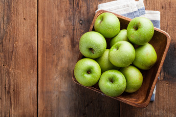 Ripe green apples in a wooden bowl on an old rustic table. Useful fruits on wooden background. Top view with copy space