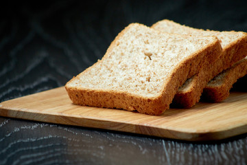 Sliced bread on wooden cutting Board, on dark wooden background, bran