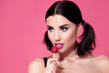 Close portrait of sexy beautiful woman brunette hair style perfect bright makeup mascara pink lipstick background face care cosmetic accessory jewelry sweets lollipop diet beauty salon white teeth.