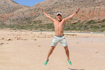 Horizontal portrait of a young man on vacation, happy jumping up on the beach. copy space