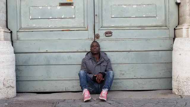 sad and depressed young African migrant sitting in the ground