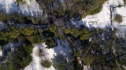 Aerial view of a dirt country road. Around the trees, bushes and grass are covered by snow. Because of the weather there is nobody in this large city park.