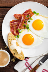 Fried eggs, bacon and italian ciabatta bread on white plate. Cup of coffee. Breakfast. Top view. Wooden background