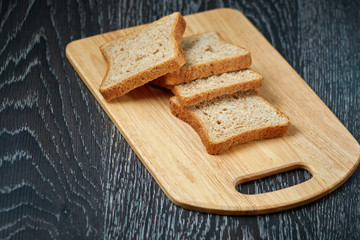 Sliced bread on wooden cutting Board, on dark wooden background, bran