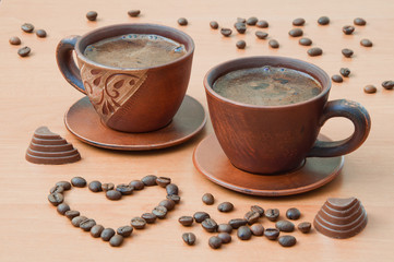 Two cups of coffee with coffee beans in the shape of a heart on a wooden table
