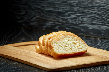 Sliced bread on wooden cutting Board, on dark wooden background, bran