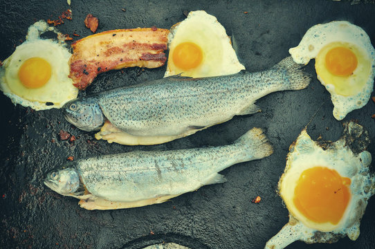 Frying fresh trout with eggs and bacon
