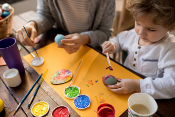 Portrait of adorable little boy painting Easter eggs while making decorations for Easter holiday, copy space