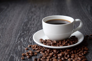 White Cup of black hot coffee with coffee beans on dark wood background