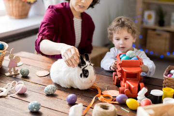 Naklejka premium Mother and cute little boy playing with bunny and toys while celebrating Easter at home, focus on foreground, copy space