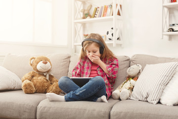 Little girl in headphones with tablet at home