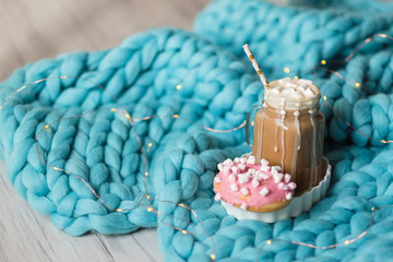 Pink donut with marshmallow and hot chocolate in glass cup on blue merino knit blanket. Lights on background