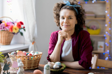 Portrait of pretty young woman smiling happily looking at camera while posing with basket of colorful Easter eggs at home, copy space