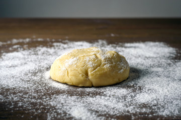 Raw dough ball sprinkled with white flour on a wooden table.