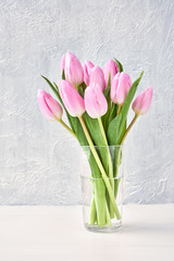 Pink tulips bouquet in glass vase on white table. Copy space