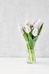 White tulips bouquet in glass vase on white table. Copy space