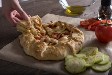 women's hands cut fresh vegetable pie with zucchini, tomatoes and cheese