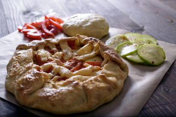 freshly baked Galeta with vegetables and cheese on a wooden table with ingredients, olive oil, red pepper, tomatoes and raw dough
