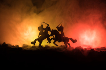 Medieval battle scene with cavalry and infantry. Silhouettes of figures as separate objects, fight between warriors on dark toned foggy background. Night scene.