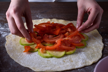 front view of the process of cooking vegetable biscuits, pizza. women's hands lay out red tomatoes on a rolled dough