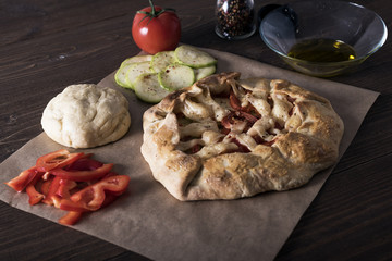 freshly baked Galeta with vegetables and cheese on a wooden table with ingredients, olive oil, red pepper, tomatoes and raw dough
