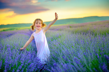 Fototapeta na wymiar beautiful little girl is walking and having fun on the lavender field at sunset