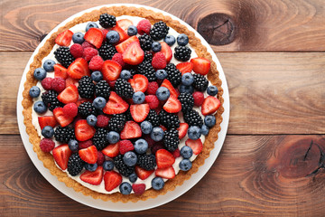 Sweet tart with berries in plate on brown wooden table