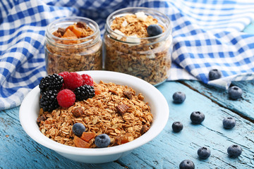 Tasty granola and berries in bowl on blue wooden table