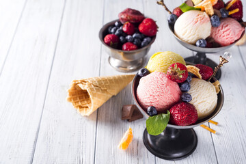 Bowl with ice cream with three different scoops of white, yellow, red colors and waffle cone, chocolate, tangerines and straws