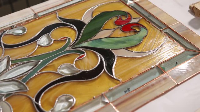Complete assembled multicolored stained-glass is in a workshop of craftsman. Camera is moving over lying decoration for windows and walls.