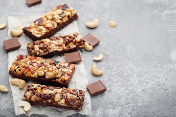 Tasty granola bars with different nuts and chocolate pieces on grey wooden table