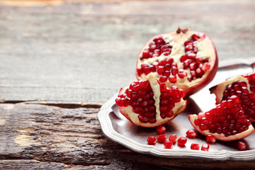 Ripe and juicy pomegranate in tray on grey wooden table