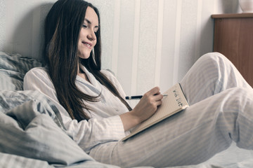 Brunette in blue pajamas lies in bed in the morning and makes a wish list