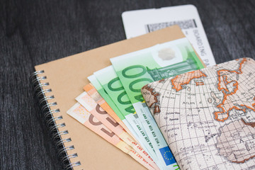 Euro banknotes on notepad and boarding pass. The money is on the craft notepad with map and airlines ticket.
