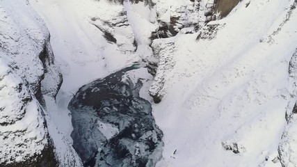 Slow aerial shot flies around a corner of a snowy canyon with a river below. Cold and frozen winter landscape. - Powered by Adobe