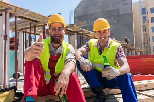 Two young workers smiling, while drinking a cold alcoholic or non-alcoholic beer during break at work on the construction site in a sunny day of summer