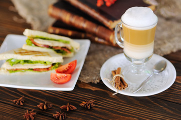 sandwiches with chicken, tomato and salad on a wooden background on a background of latte and old books close-up