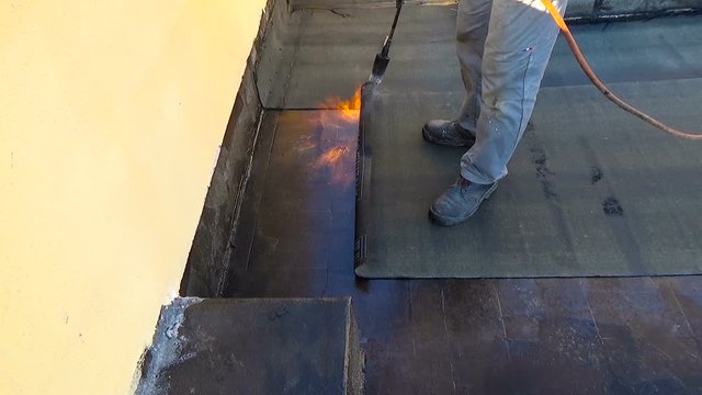 Worker preparing part of bitumen roofing felt roll for melting by gas heater torch flame. On the back of the sheath there is the stamp  "Made in Italy" product