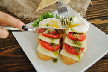 breakfast bread with egg poached, tomato, cheese and greens close-up on a wooden background