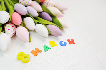 inscription from color letters - March 8 against a background of toy tulips flowers on a white wooden background