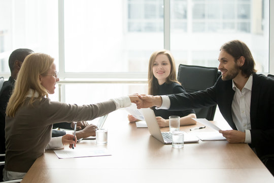 Smiling businessman and businesswoman shaking hands over conference table, company executive welcoming new business partner at diverse team meeting, gender equality business handshake concept