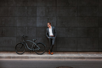 Stylish young businessman in sunglasses stands near a bicycle