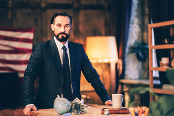 Half length image of smart enterpreneur standing at desk. USA flag behind.