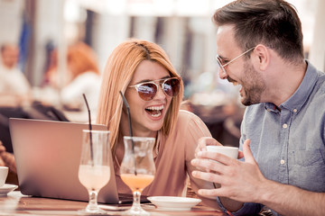 Happy couple in coffee shop using laptop and drink coffee.