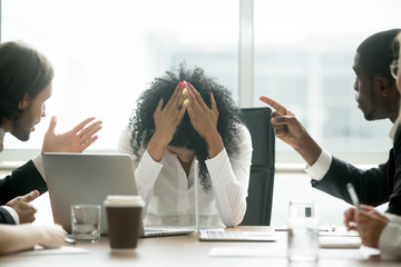 Upset depressed black woman leader suffering from gender discrimination inequality at work, diverse men colleagues pointing fingers scolding bullying frustrated african businesswoman at workplace - obrazy, fototapety, plakaty