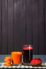 Natural juices from carrots and beets. The juice is poured into a clear glass, which stands on a tablecloth, next to sliced carrots and beets. Tasty and healthy juice.