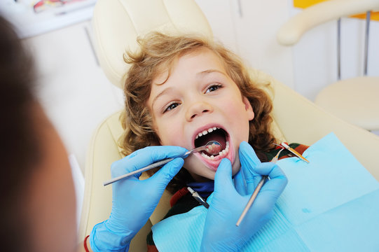 A cute, curly-haired child indulges and grimaces in a dental chair