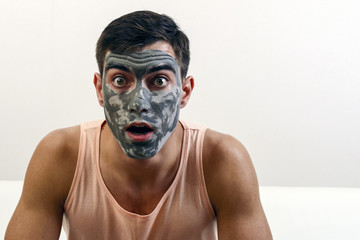 surprised portrait of a man in a clay mask on his face. skin care. copy space